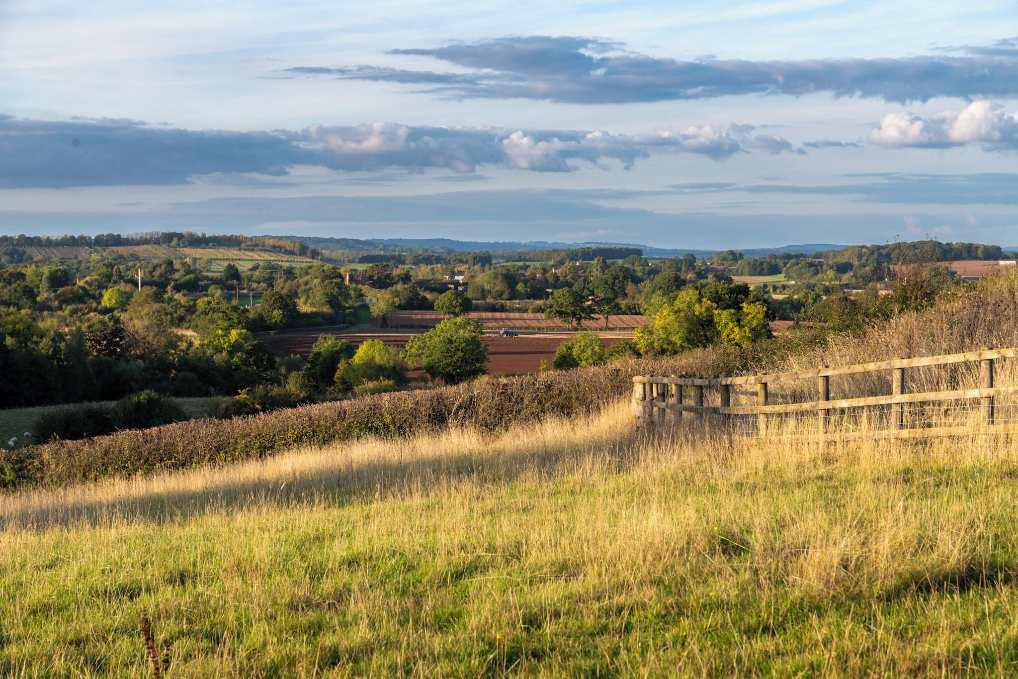 A rural landscape with fields, trees, and a distant view of hills.