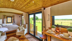 Una camera da letto con un letto, un divano, un tavolo da pranzo con sedie e vista su un paesaggio verde attraverso ampie finestre.