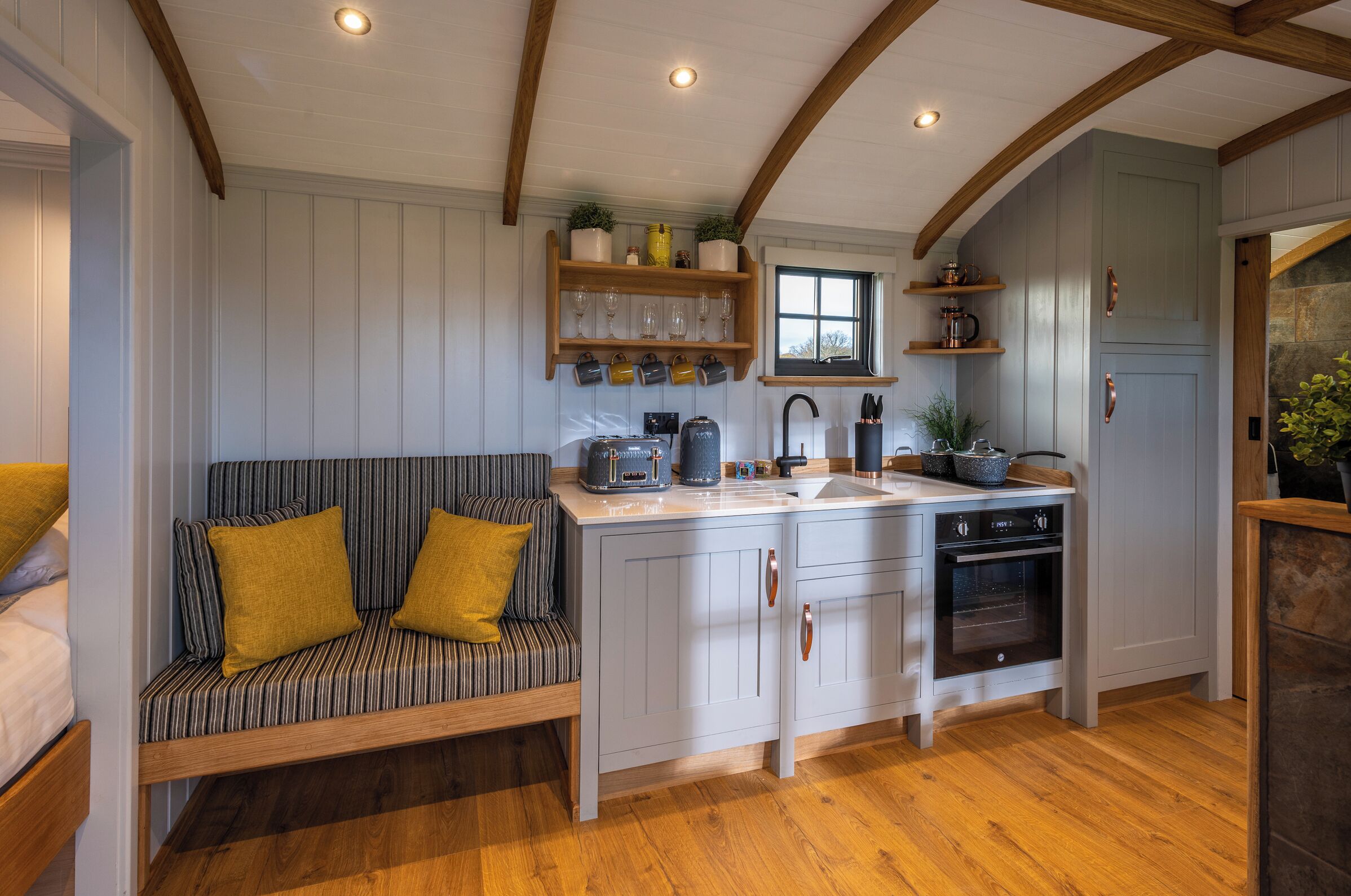 A kitchen with wooden beams, a built-in bench with cushions, a sink, and a stove.