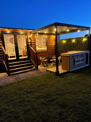A wooden cabin with a glass door entrance, a covered outdoor seating area, and a sign reading "GARDEN BAR".