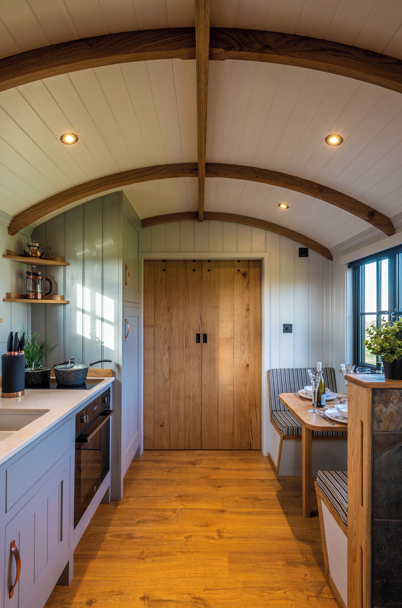 A kitchen with wooden beams, a central door, and a dining area with a table and chairs.