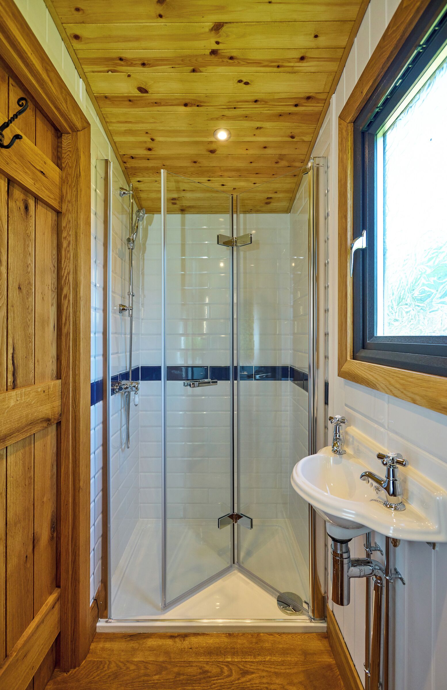 Une douche avec des portes en verre, un lavabo blanc et un lambris en bois.