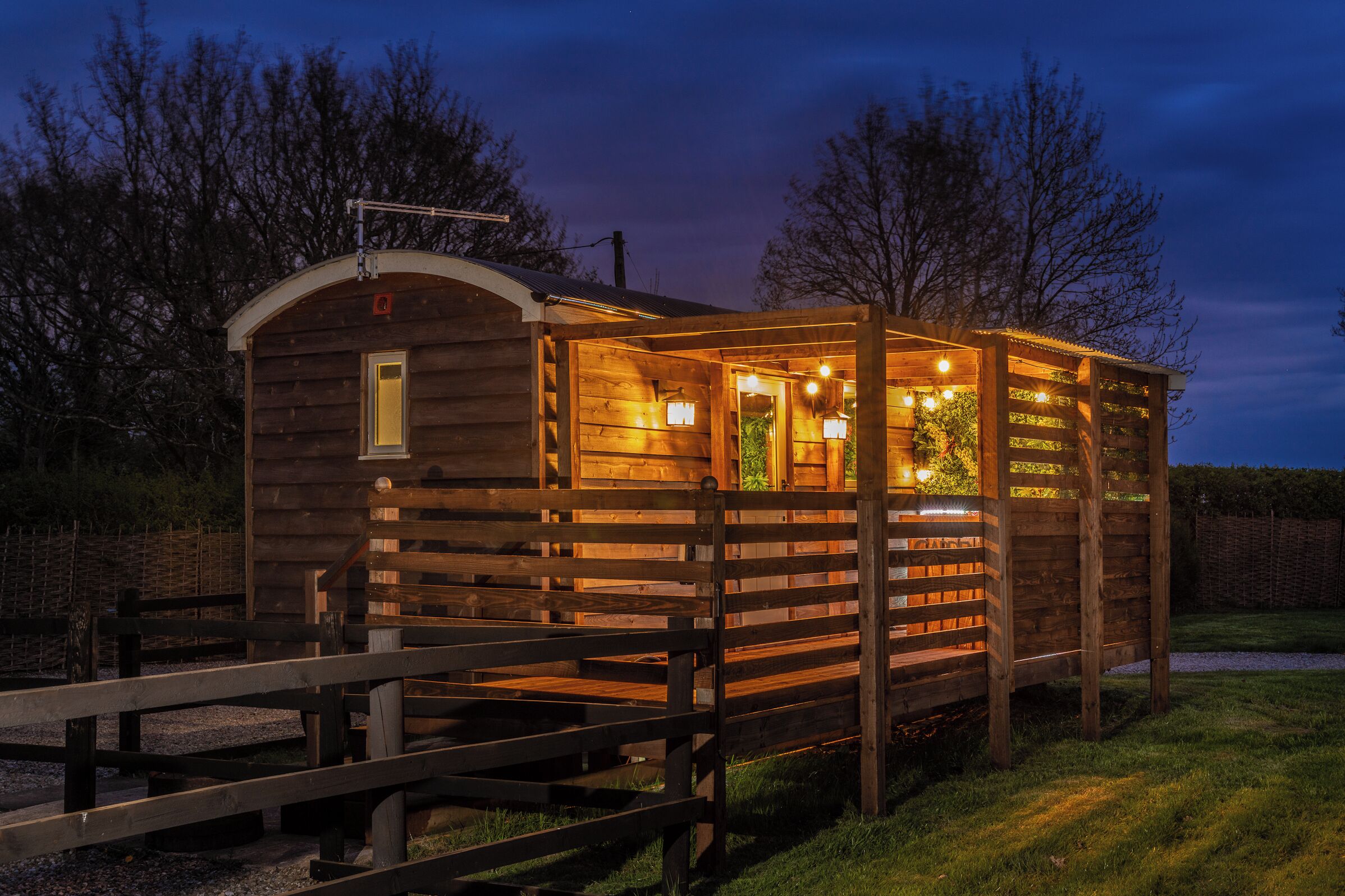A wooden cabin with a porch and a small attached structure, both illuminated by warm lighting.