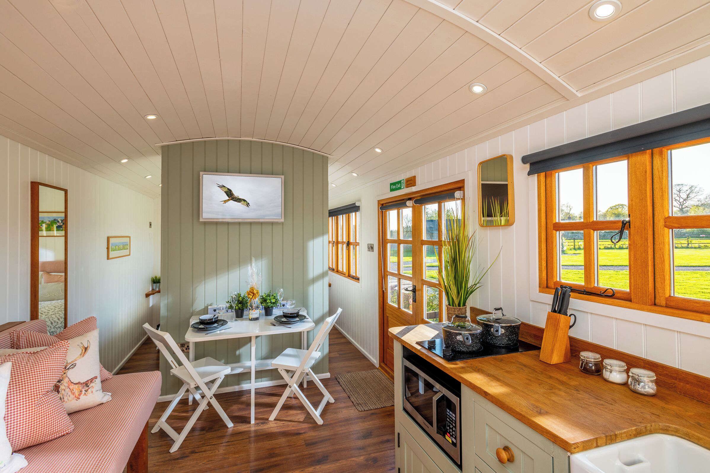 A cozy room with a dining area, a kitchen with a window view, and a bed with a checkered blanket.