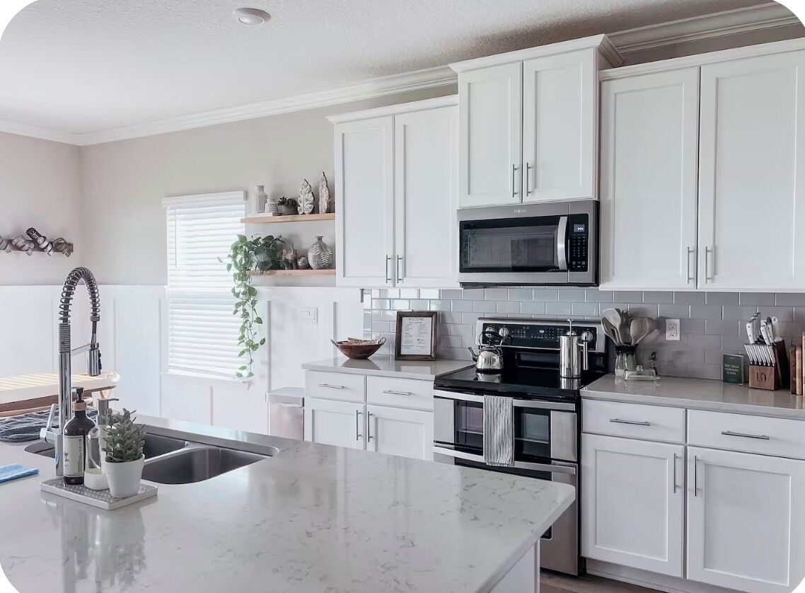 Una cocina moderna con armarios blancos, estufa negra, microondas y una isla grande con pileta.
