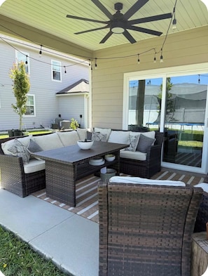 Eine überdachte Terrasse mit Korbmöbeln, einem Deckenventilator und Lichterketten.