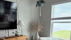 A living room with a television, a lamp, a chair, a couch, a rug, and a window with a view. - Organic Modern Home, Close to the Beach & Downtown. Community Pool & gym (St. Augustine)
