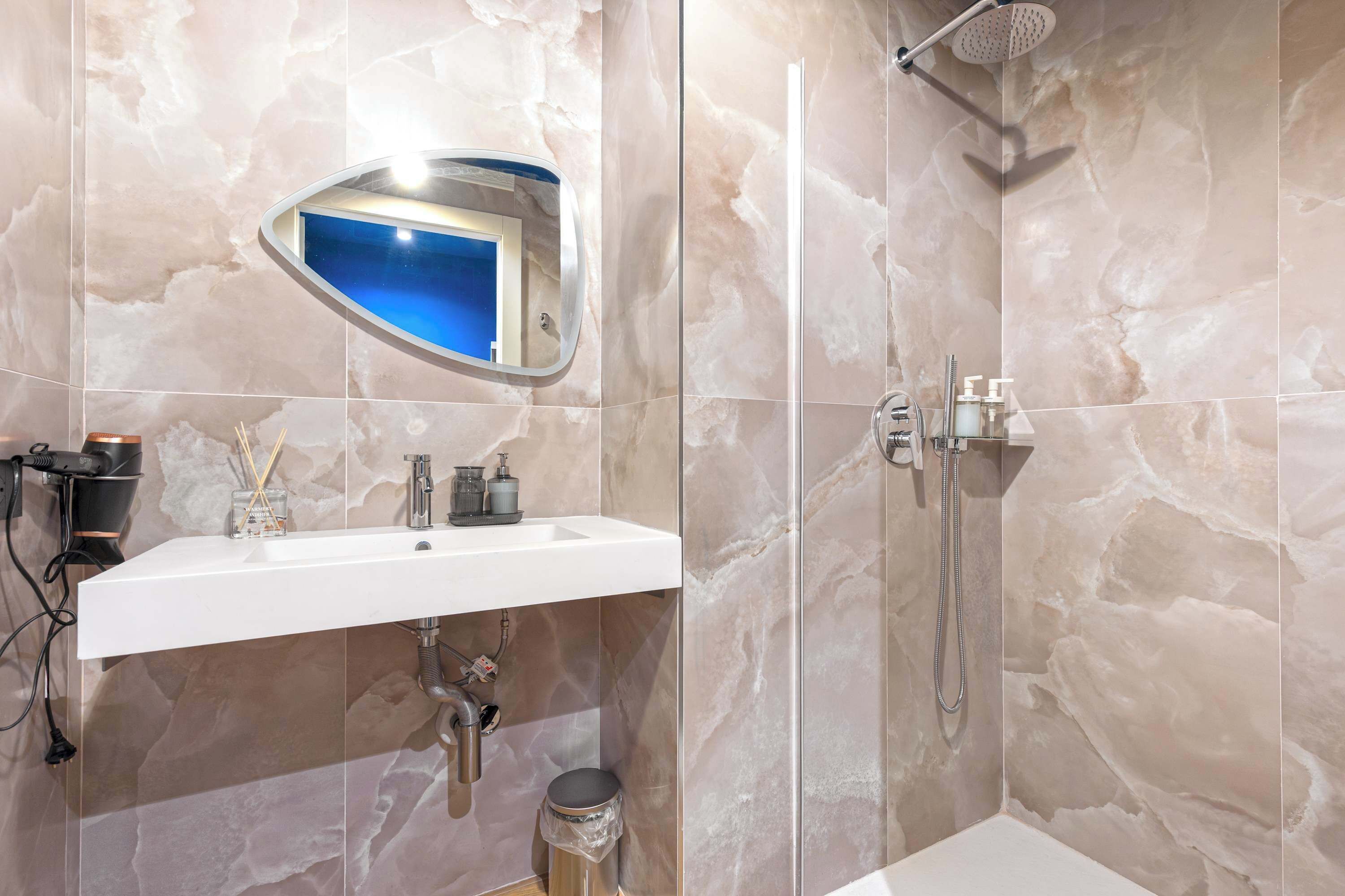 Une salle de bain avec un lavabo blanc, un miroir, une douche et des murs en marbre.