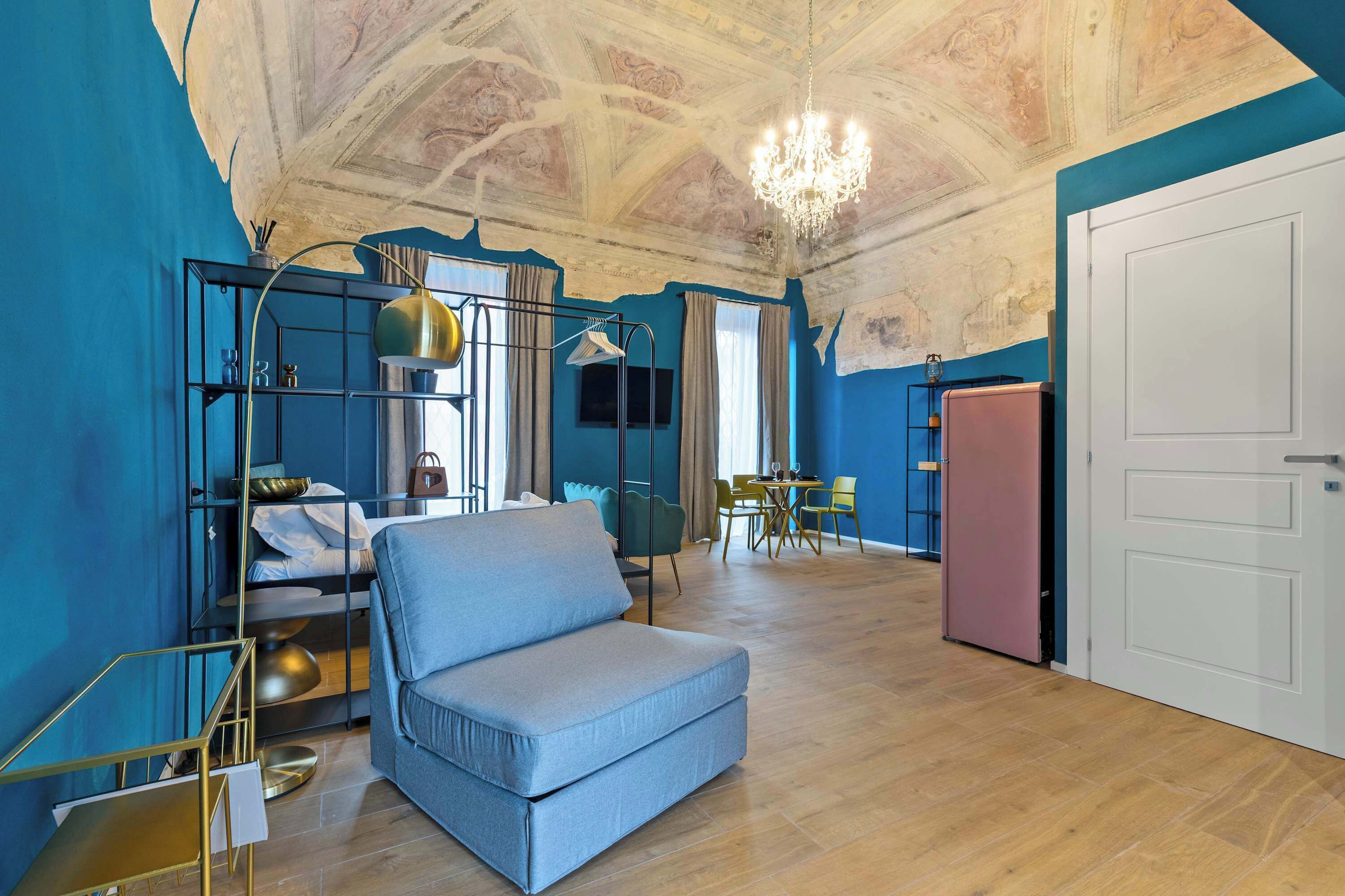 Ein Zimmer mit blauer Wand, einer Couch, einem Kronleuchter, einem Essbereich und einer Tür.