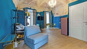 Una habitación con pared azul, un sofá, una araña y un comedor, además de una puerta.
