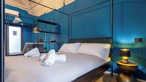 Una habitación de hotel moderna con una cama grande, una mesita de noche con lámpara, un armario y un espejo.