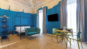 Ein Zimmer mit einem Bett, einem Hängesessel, einem Esstisch mit Stühlen, einem an der Wand montierten Fernseher und einer Decke mit Fresken.