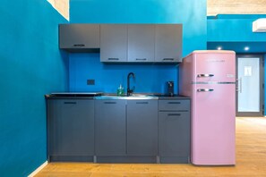 Una cocina moderna con armarios grises, un refrigerador rosa y una pared azul.