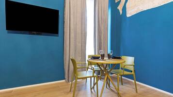 Une pièce avec un mur bleu, un téléviseur à écran plat, une table à manger avec des chaises et une fenêtre avec des rideaux.