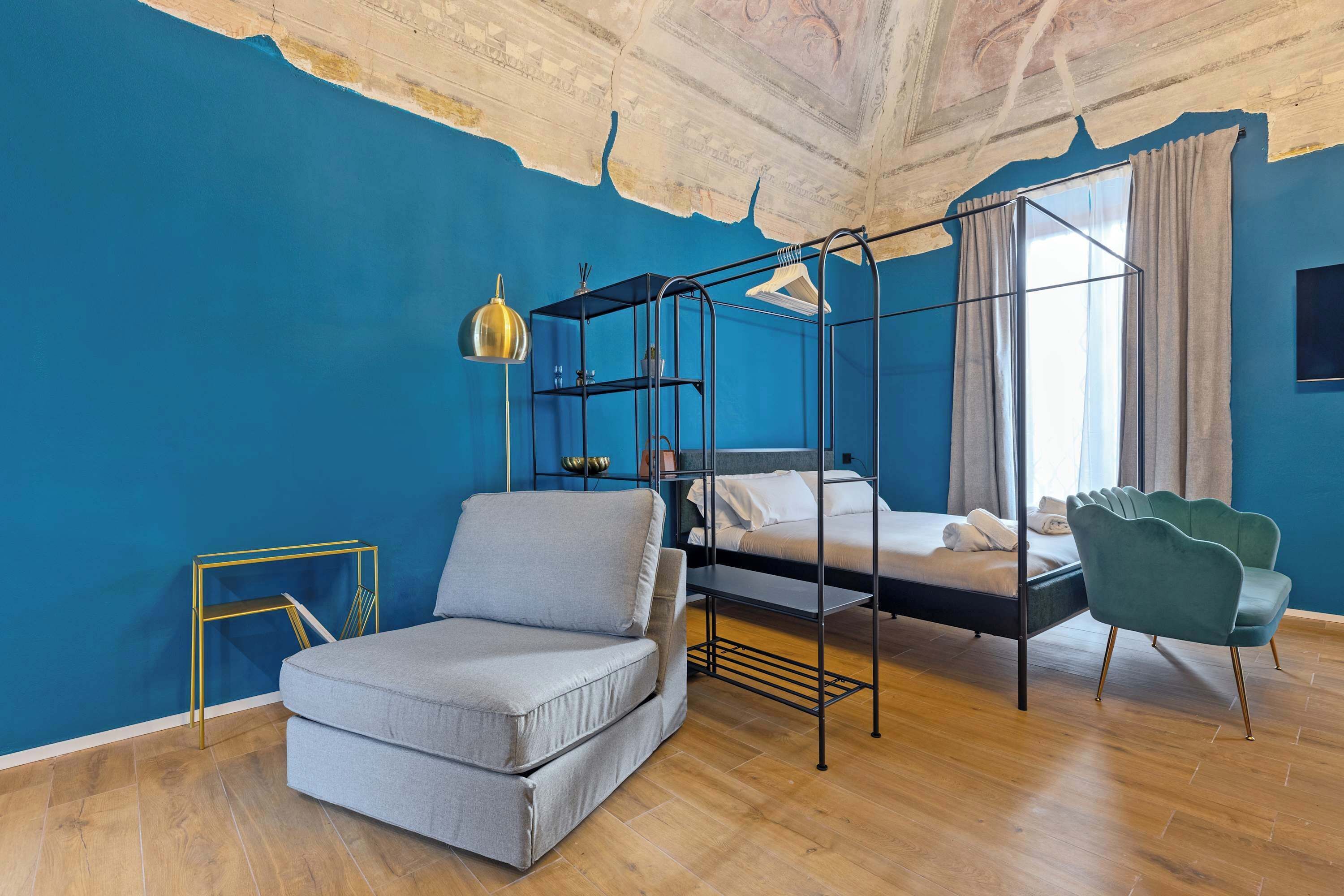 Una habitación con cama, sofá, sillón, lámpara colgante y techo con vigas a la vista.