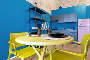 Un comedor con una mesa y sillas amarillas, una cocina con armarios azules y un refrigerador rosa.