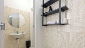 Ein Badezimmer mit Waschbecken, Spiegel, gefliesten Wänden und Ablagen für Pflegeprodukte.