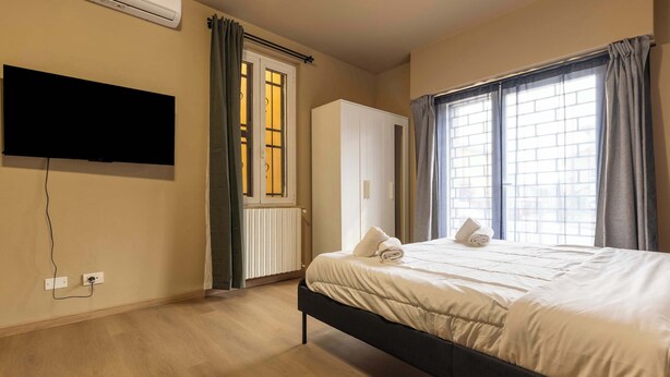 Ein Schlafzimmer mit Bett, Kleiderschrank, Fernseher und einem Fenster mit Vorhängen.