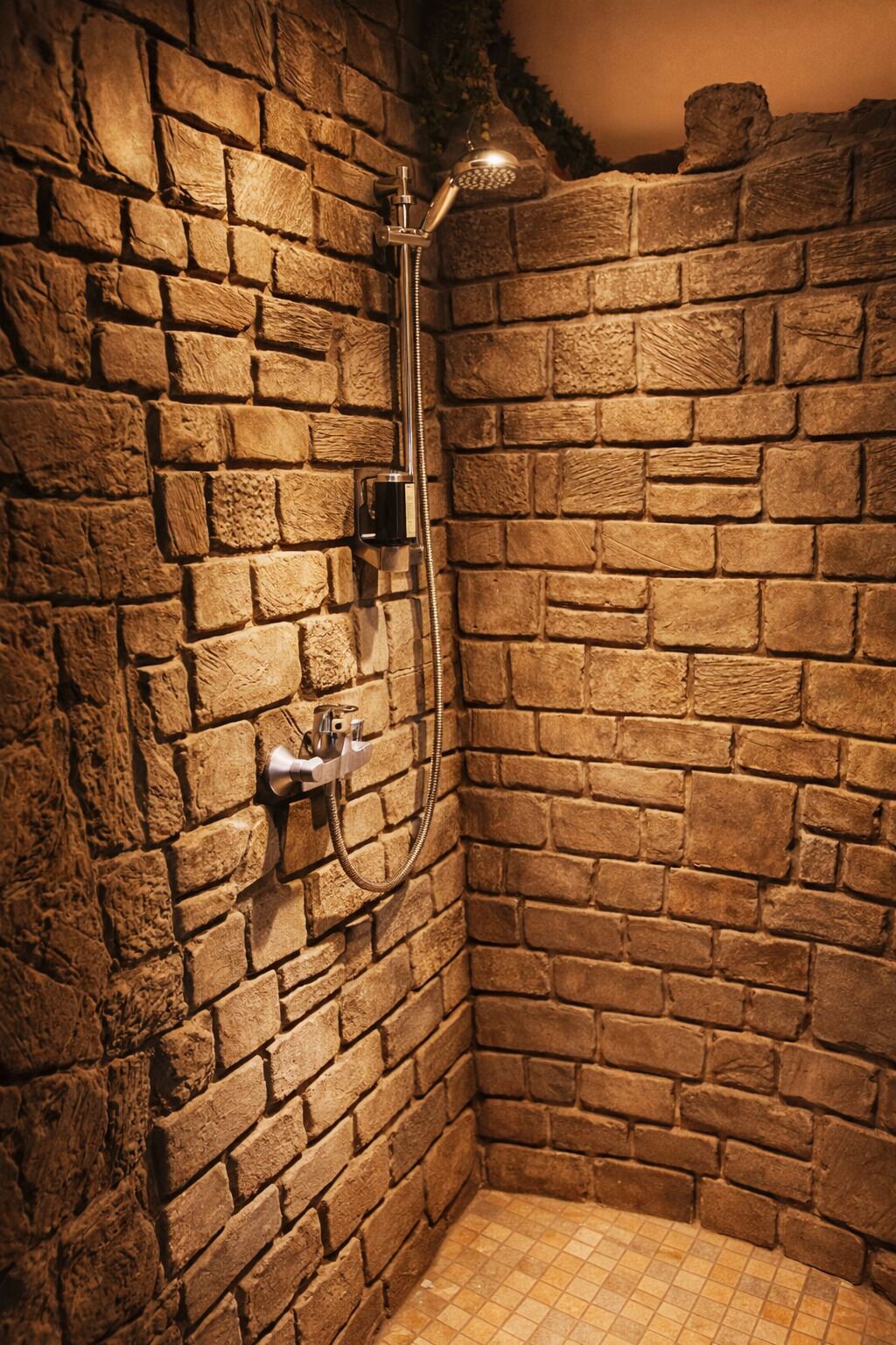 A stone-walled shower with a handheld showerhead and a wall-mounted faucet.
