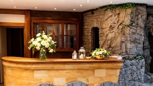 A reception area with a stone counter, a wooden door, and a stone wall with greenery. - ALPRESORT Hubertushof (Oberstaufen)