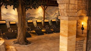 A spa area with stone pillars, reclining chairs, and a mural of mountains. - ALPRESORT Hubertushof (Oberstaufen)