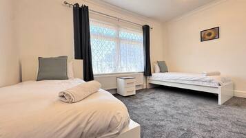 Une chambre avec deux lits, un radiateur, un bureau et une fenêtre avec des rideaux.