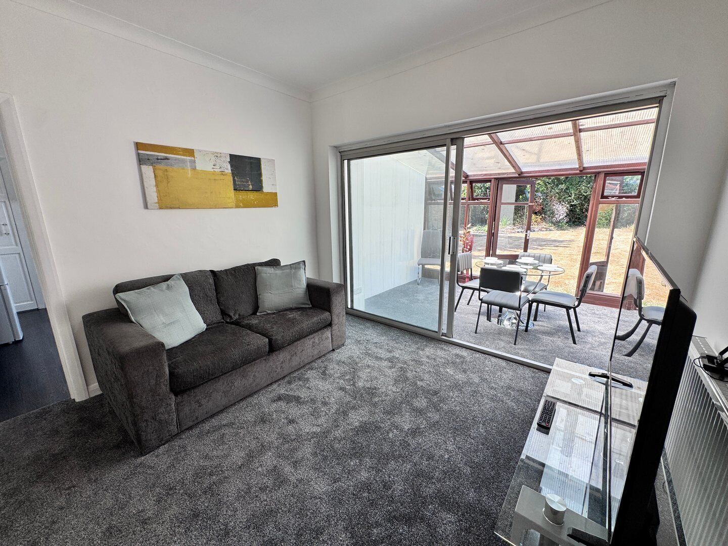 Un salón moderno con un sofá gris, un ventanal de vidrio que da a un patio exterior con una mesa y sillas.