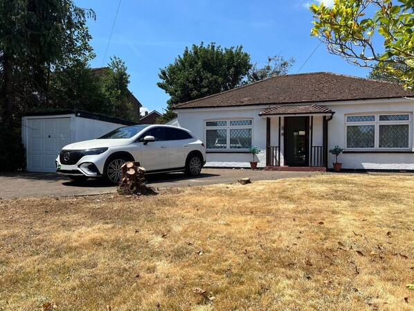 Ein weißes Auto parkt vor einem Haus mit Garage, einer kleinen Veranda und einem Blumentopf.