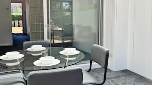 Ein Essbereich mit Glastisch und Stühlen, eine Glasschiebetür zum Garten hin und ein Blick auf einen Hinterhof.