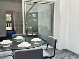 Comedor con mesa y sillas de vidrio, puerta corrediza de vidrio que da al exterior y vista a un patio trasero.