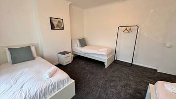 Un dormitorio con dos camas, una mesita de noche, un mueble pequeño y un perchero en la pared.