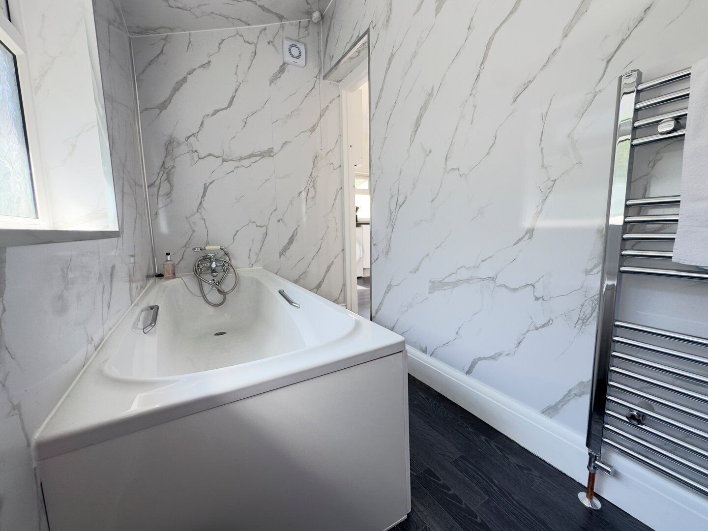 A modern bathroom with a marble wall, a freestanding bathtub, and a towel rack.