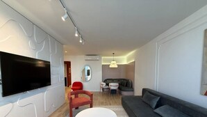 Een moderne woonkamer met een flatscreen televisie, een ronde salontafel, een grijze bank en een rode fauteuil.