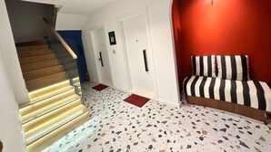 Een trap met glazen leuning die uitkomt op een plateau, een rode accentmuur en een gestreepte bank.