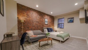 A modern room with a brick wall, a bed, a sofa, a small table, and a desk. - Modern Simple Studio | South End (Boston)