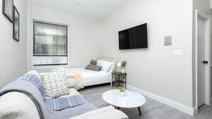Quarto moderno com cama, mesa de cabeceira, televisão e janela com persianas.