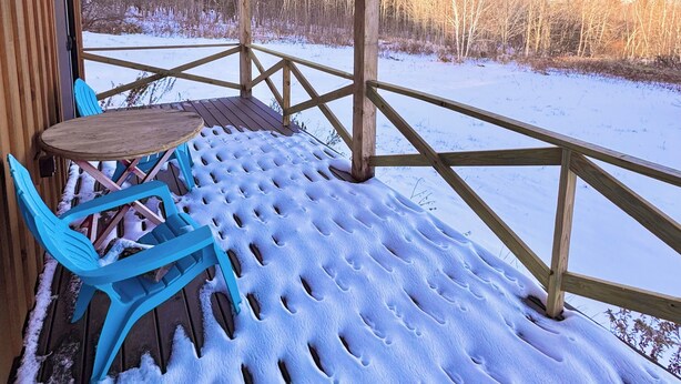 A covered outdoor seating area with a table and chairs, wooden beams, and a view of a snowy landscape. - Cute 2-bedroom house in Jay, perfect for a relaxing getaway. (Jay)