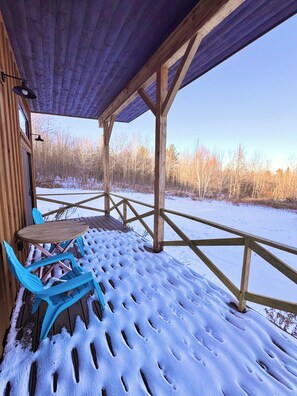 Un área de estar al aire libre techada, con una mesa y sillas, vigas de madera y vistas a un paisaje nevado.
