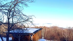 A wooden cabin with a sloped roof, surrounded by snow-covered ground and leafless trees, set against a clear blue sky. - Cute 2-bedroom house in Jay, perfect for a relaxing getaway. (Jay)