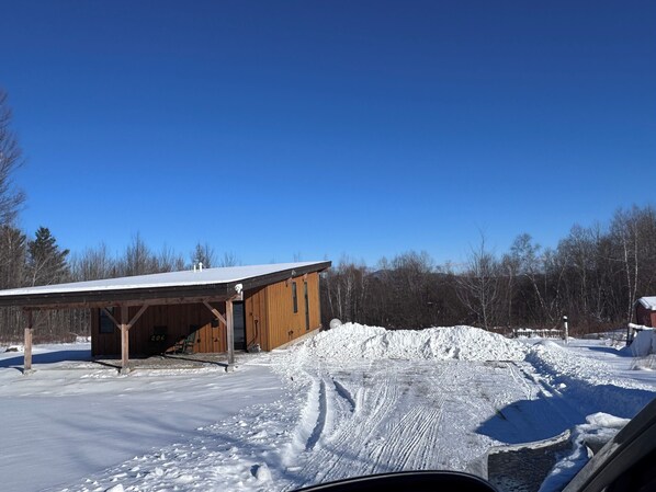 A wooden building with a covered porch, a snow-covered ground, and a clear blue sky. - Cute 2-bedroom house in Jay, perfect for a relaxing getaway. (Jay)
