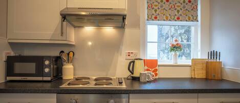 A modern kitchen with white cabinets, a Bosch microwave, a stove, and a window with a fruit pattern.