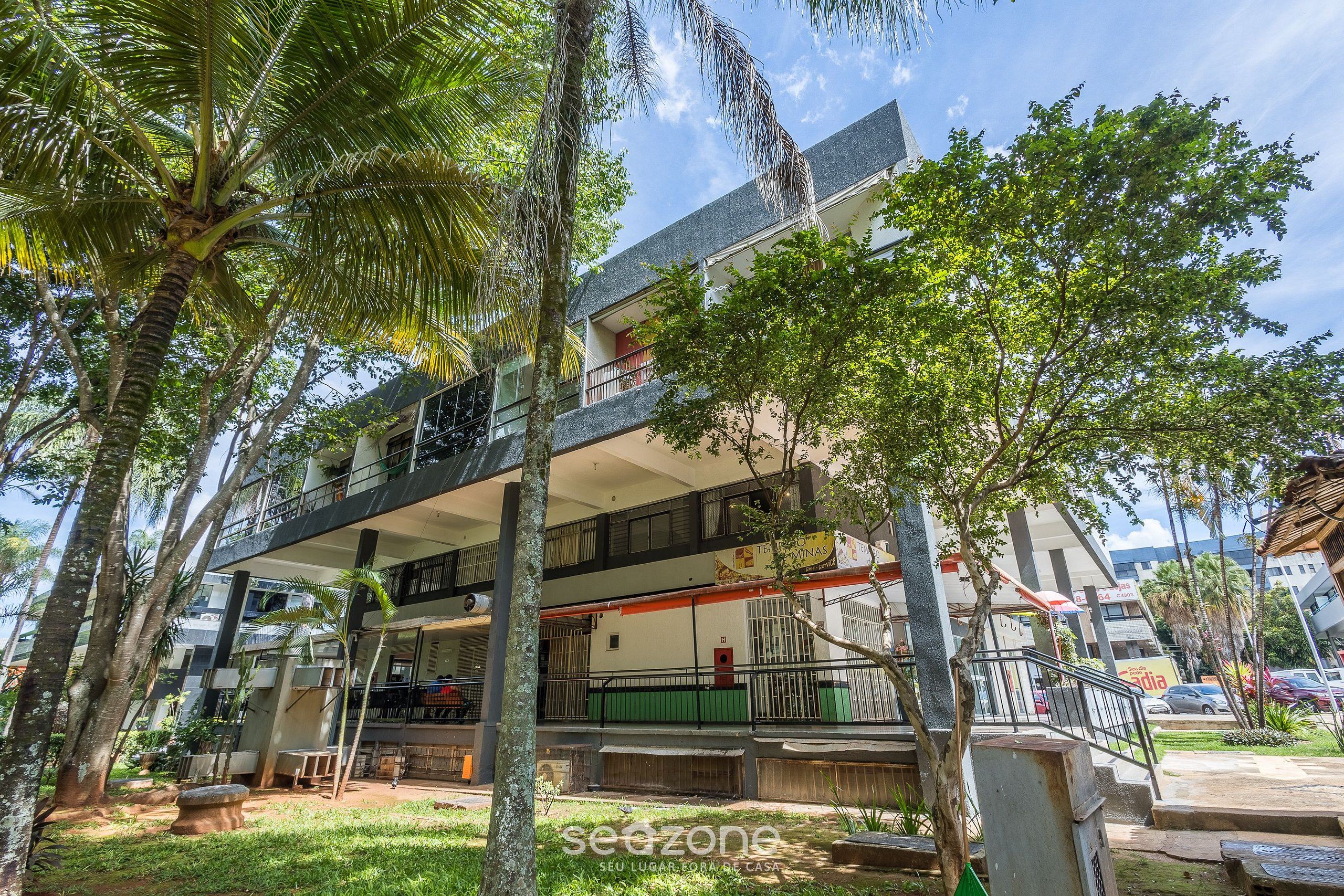 A multi-story building with balconies, surrounded by trees and greenery.