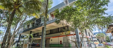 A multi-story building with balconies, surrounded by trees and greenery.