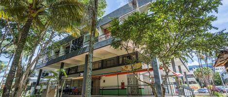 A multi-story building with balconies, surrounded by trees and greenery.