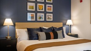 Una habitación de hotel con una cama, dos mesitas de noche, dos lámparas y una pared decorada con nueve cuadros.