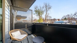 Un balcón con una silla de mimbre, una mesita redonda, mosquitero y vistas a árboles y casas.