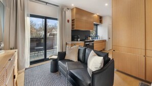 Una sala de estar moderna con un sofá de cuero negro, una mesita de centro y vistas al exterior a través de una puerta corrediza de vidrio.