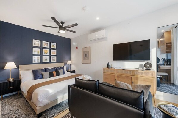 A modern hotel room with a bed, a desk, a flat-screen TV, a ceiling fan, and artwork on the wall. - Executive Studio | Refined Design + Hotel Finish (Manhattan)