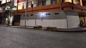 Un hôtel à plusieurs étages doté de balcons, une enseigne indiquant le prix d’une chambre individuelle, et une rue devant l’établissement.