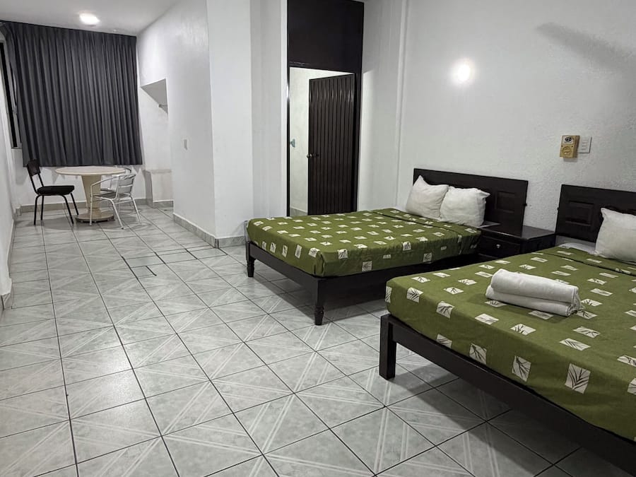 A hotel room with two beds, a small table, and a chair.